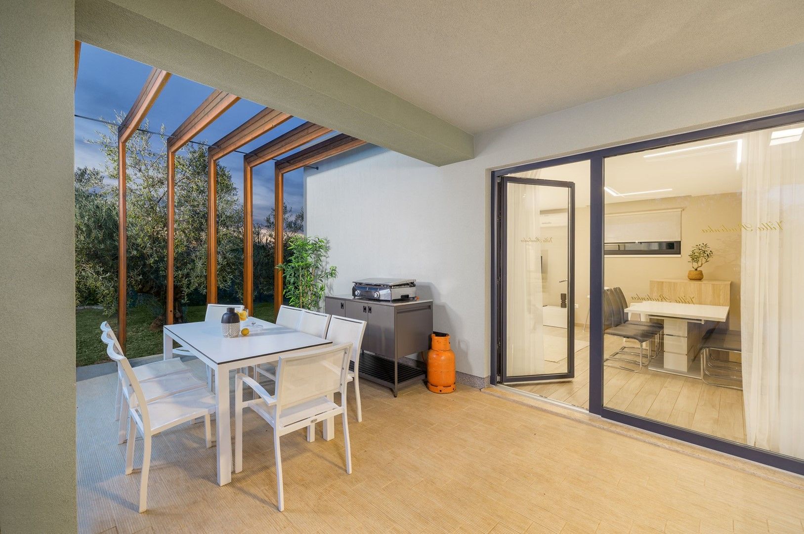 An outdoor dining area with a table and chairs, a grill, and a sliding glass door leading to an interior space.