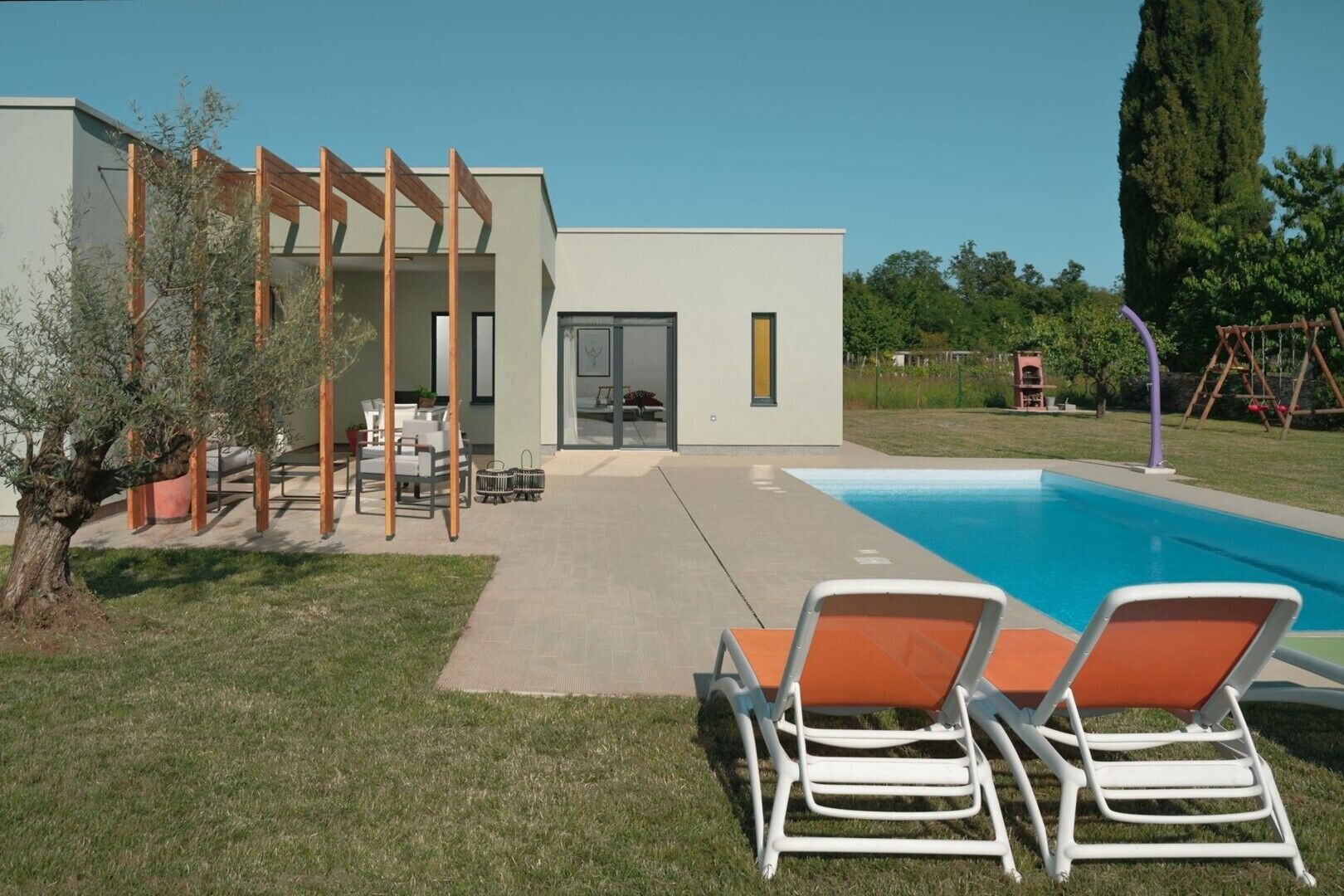 Een modern huis met een zwembad, tuinmeubilair en een pergola.