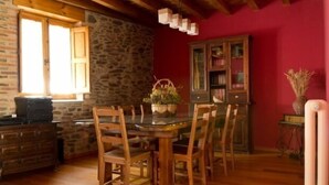 A dining area with a wooden table and chairs, a stone wall, a red wall, and a cabinet with glass doors.