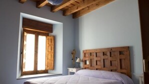 A bedroom with a wooden headboard, a window with wooden shutters, and a bedside table with a lamp.