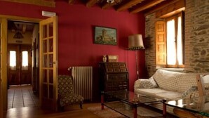 A cozy living room with a red wall, a stone wall, a wooden door, a patterned sofa, a glass coffee table, and a lamp.
