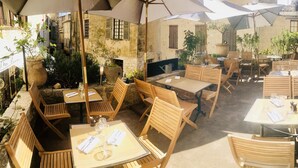An outdoor café with wooden tables and chairs, umbrellas, and potted plants. - Hostellerie la Fontaine (Saint-Paul-de-Vence)