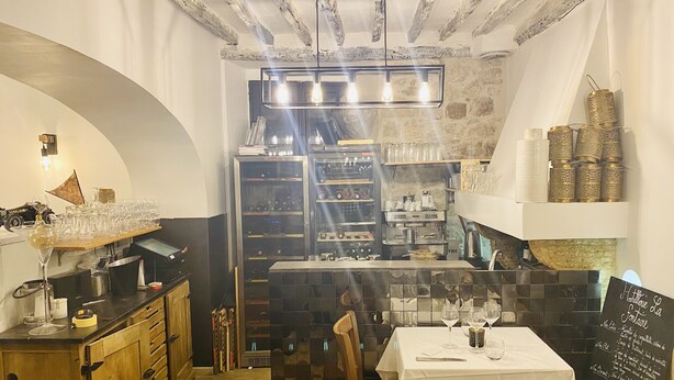 A cozy restaurant interior with a wooden counter, a white table with a menu, and a stone wall. - Hostellerie la Fontaine (Saint-Paul-de-Vence)