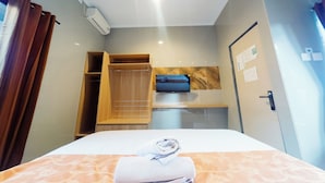 Una camera d'albergo con un letto, un armadio in legno, un piccolo ripiano con una TV e una porta con serratura.