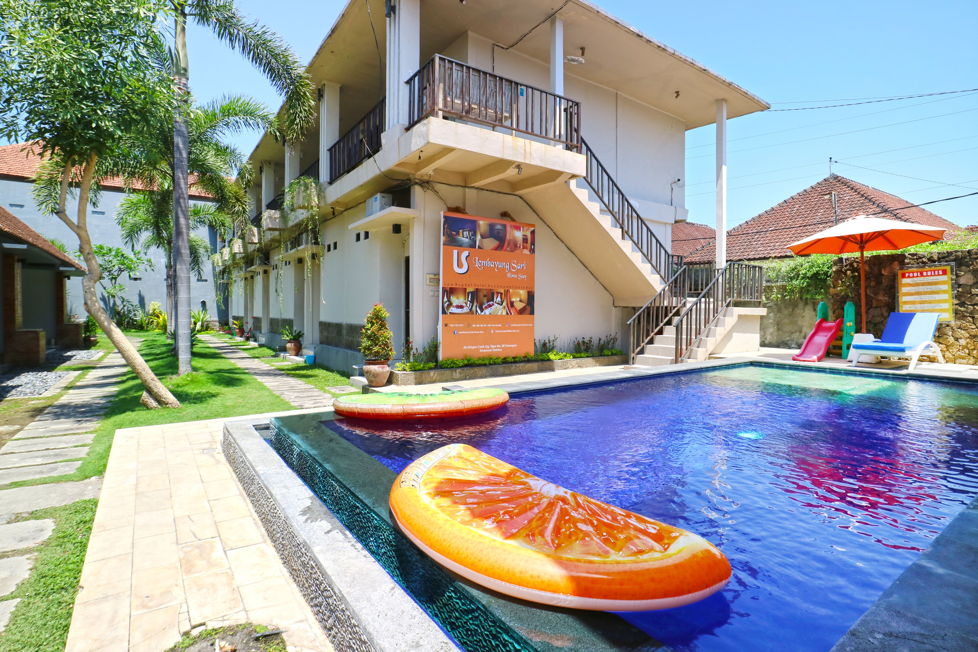 A swimming pool with a unique design, a multi-level building with a balcony, and a signboard advertising a restaurant.