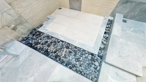 Un bagno con pavimento piastrellato, una piccola zona con pietre e un pannello decorativo a parete.