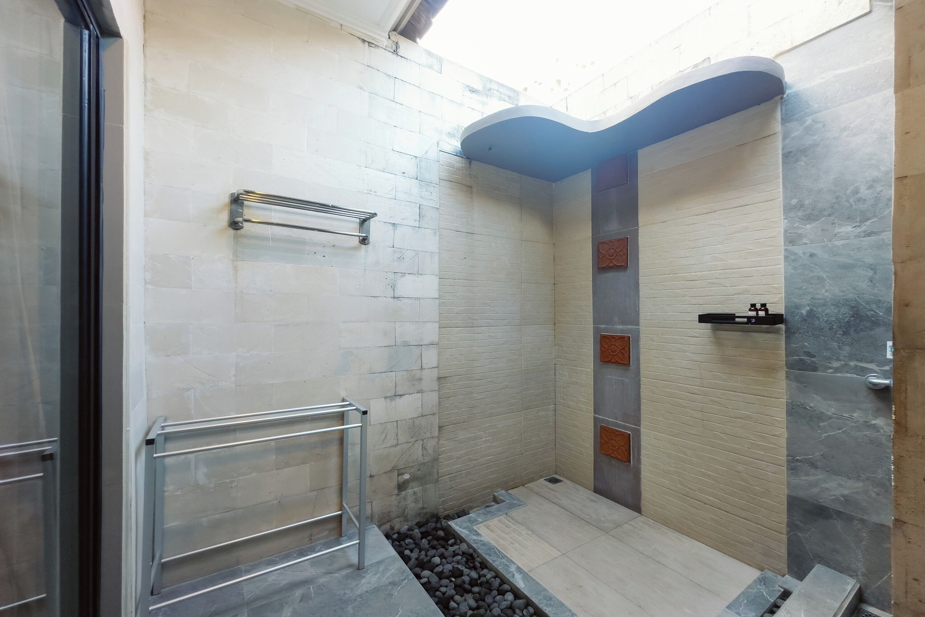 A shower area with a glass door, a metal handrail, and a tiled floor.