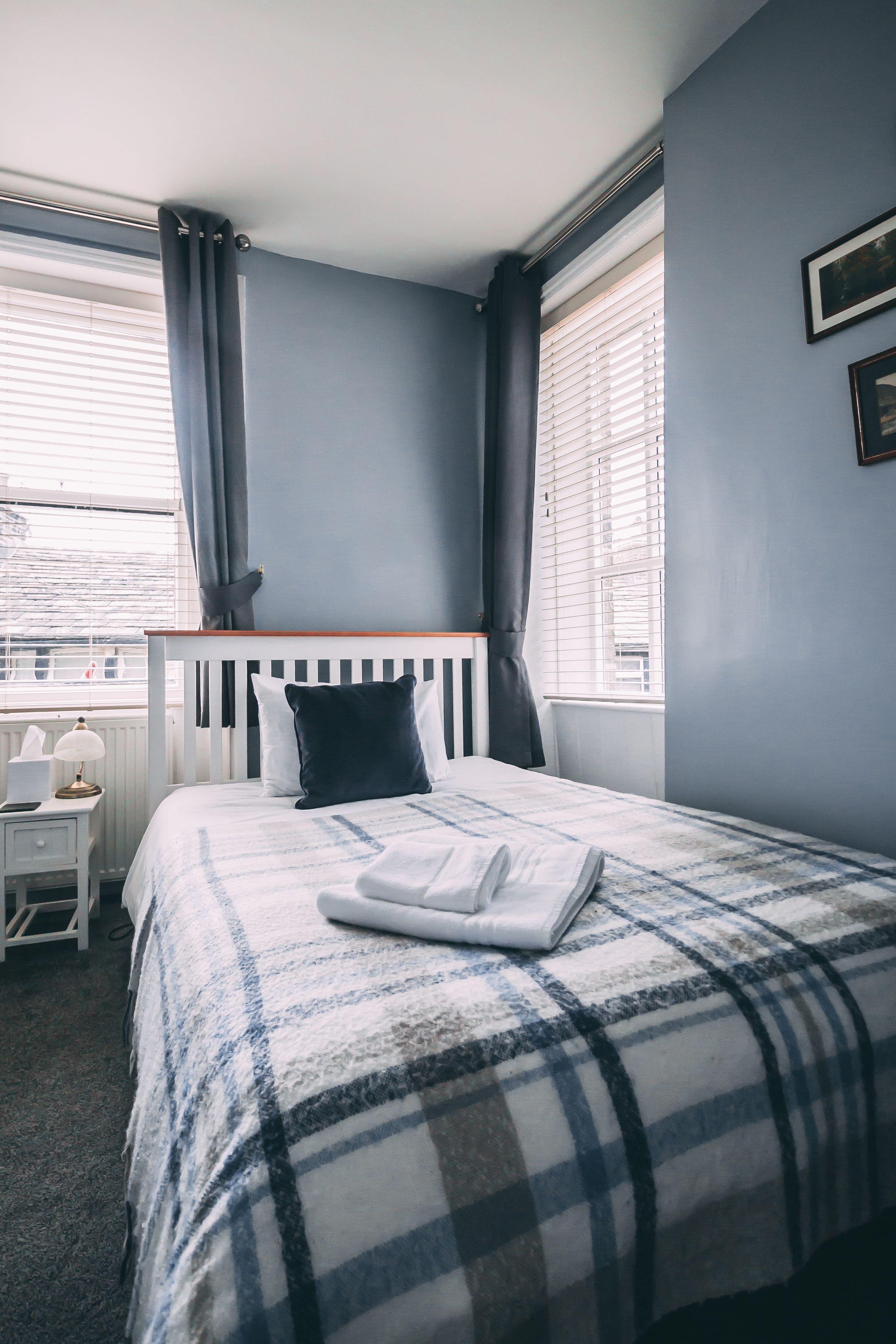 A bedroom with a bed, a nightstand, a chair, and a window with curtains.