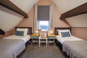 Un dormitorio acogedor en el ático con dos camas, una mesita con lámparas y una ventana con vistas.