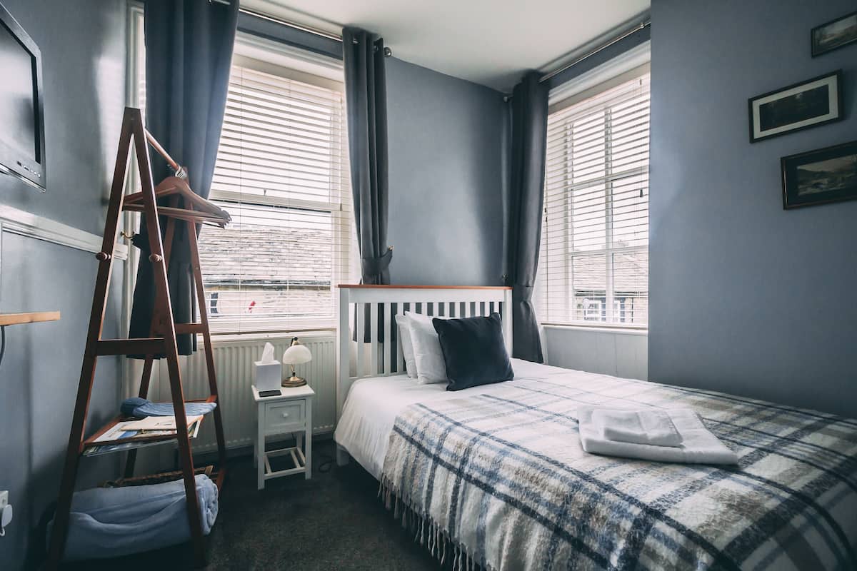 A bedroom with a bed, a wooden ladder, a nightstand, and a window with blinds.