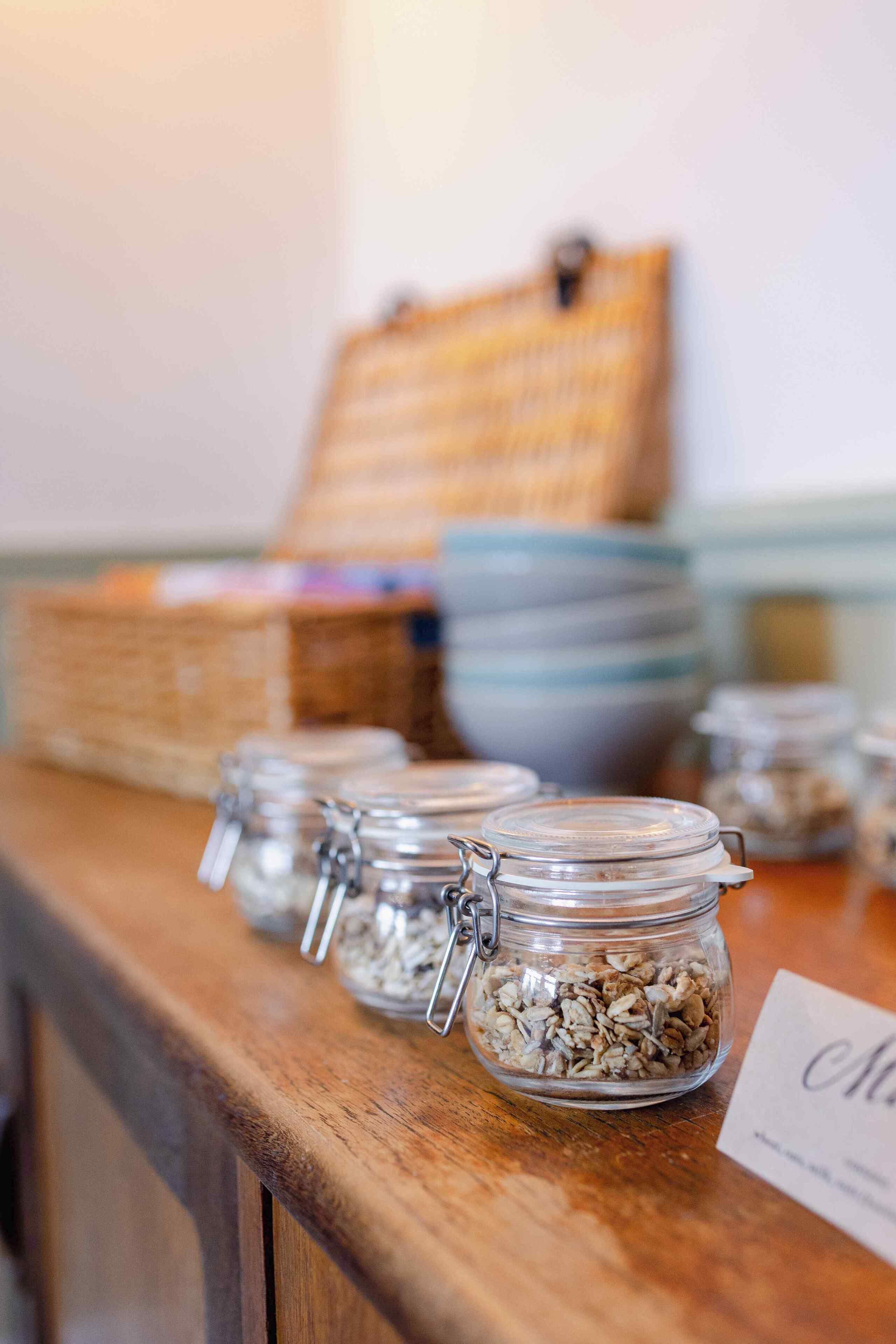 A wooden counter with glass jars containing granola, a woven basket, and stacked plates.