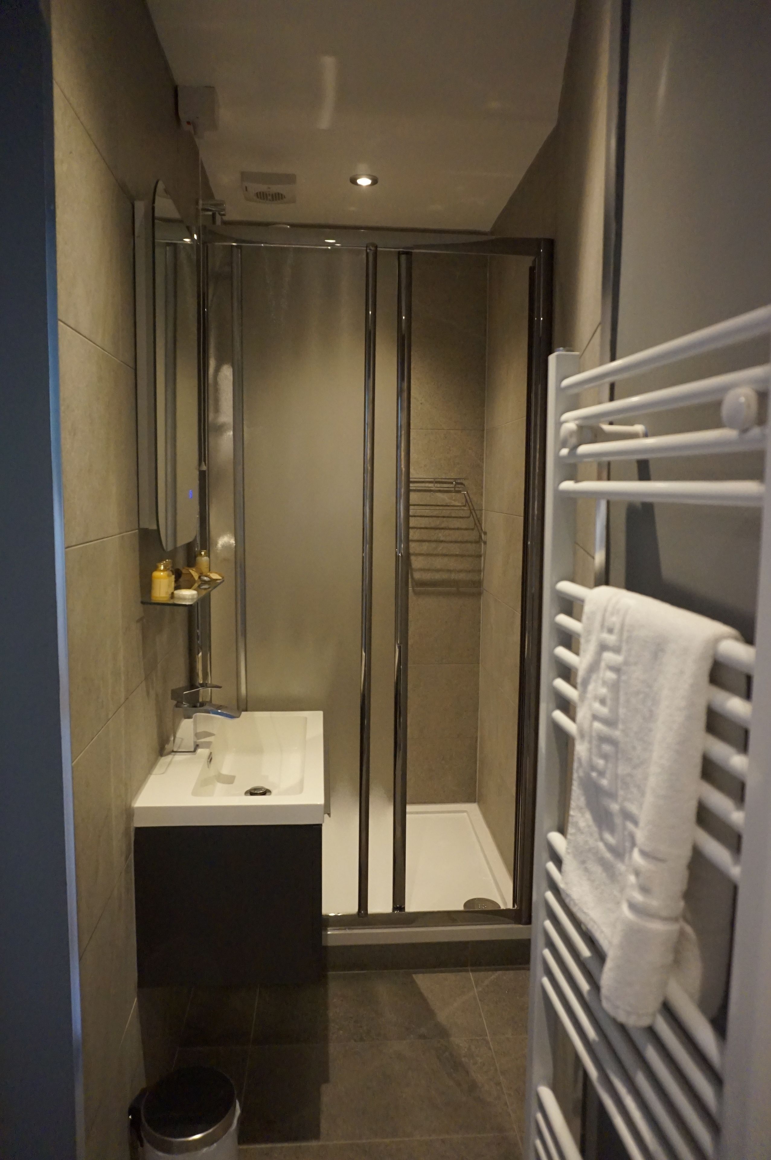 Un baño moderno con ducha de vidrio, lavamanos blanco y barra para toallas.