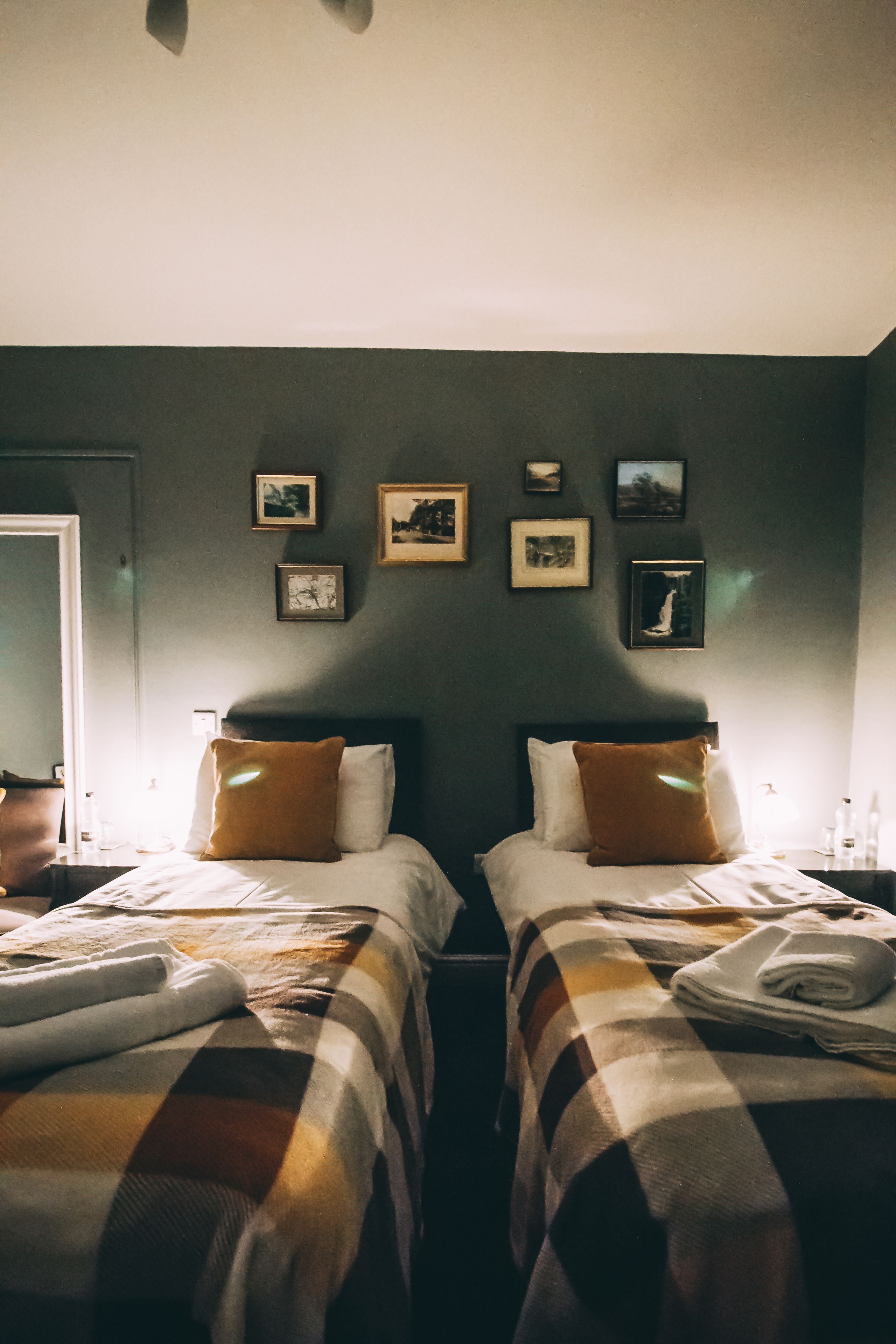 Ein Hotelzimmer mit zwei Betten, jedes mit einer karierten Decke, einem braunen Kissen und einem weißen Kissen. An der Wand über den Betten befinden sich gerahmte Bilder.
