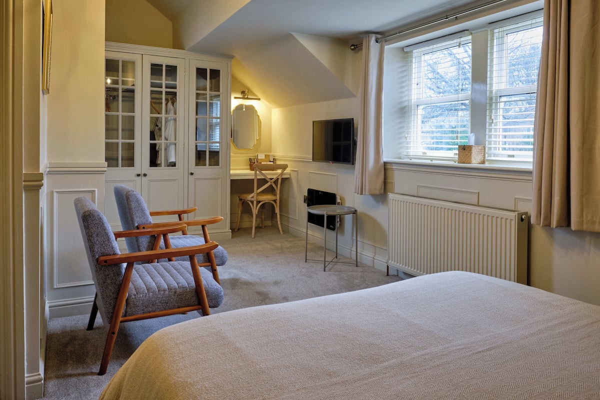 A bedroom with a large bed, a chair, a desk, a mirror, and a wardrobe.