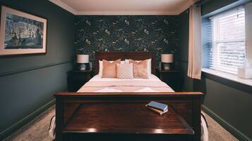 A bedroom with a large bed, two bedside tables with lamps, a framed picture on the wall, and a window with blinds.