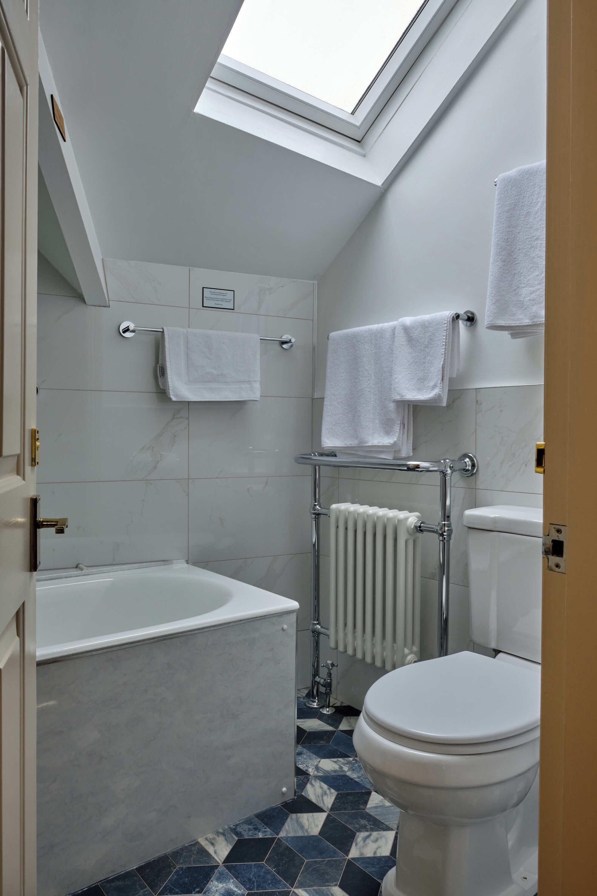 A bathroom with a skylight, a bathtub, a toilet, and a towel rack.