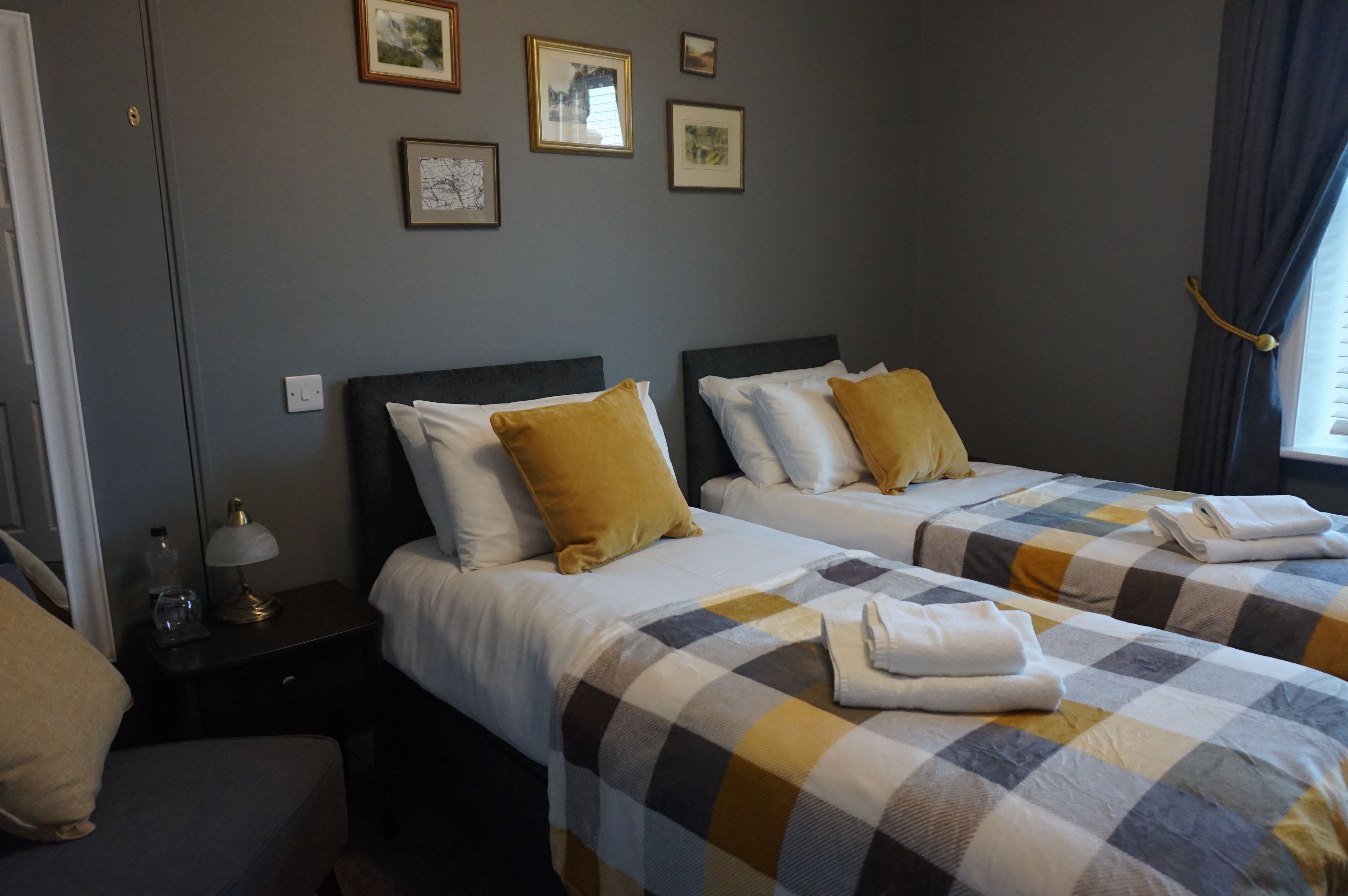 A hotel room with two beds, each with a checkered bedspread, a nightstand with a lamp, and framed pictures on the wall.