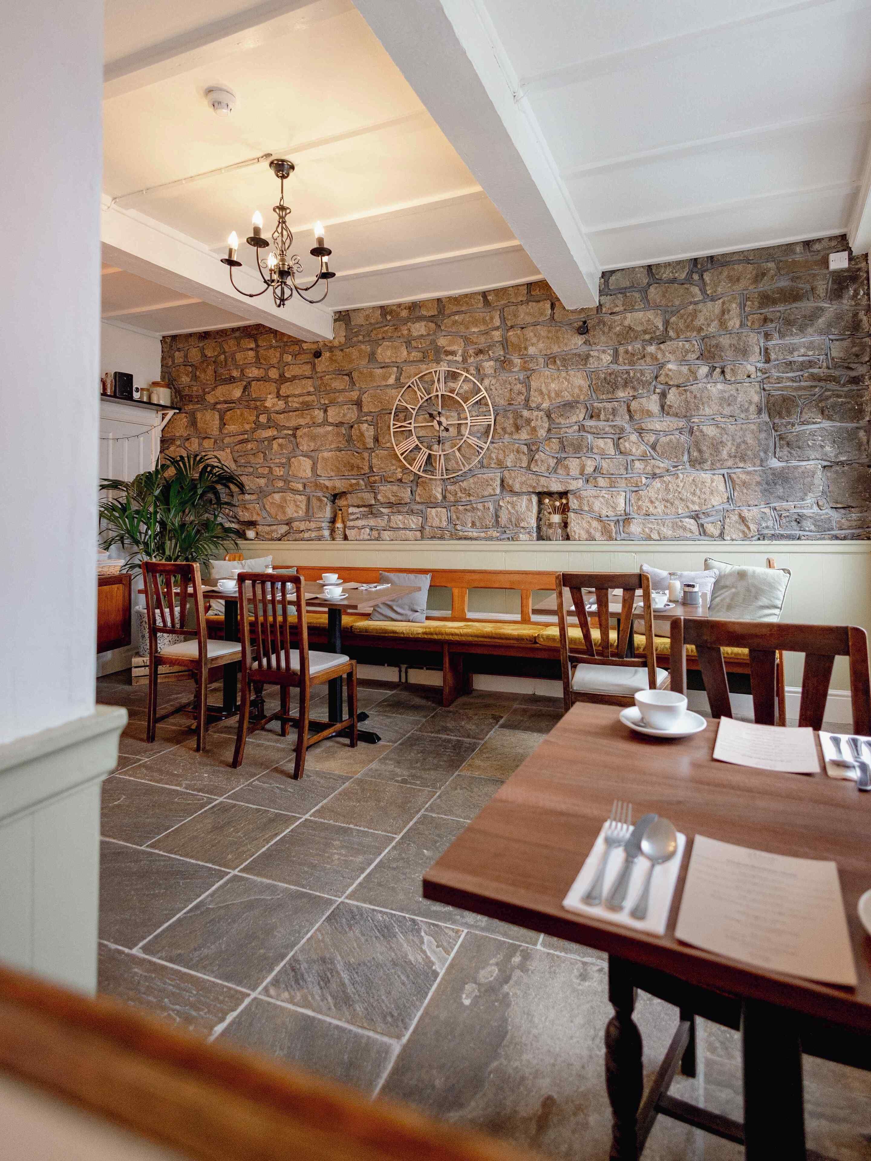 A dining area with a stone wall, wooden furniture, and a chandelier.