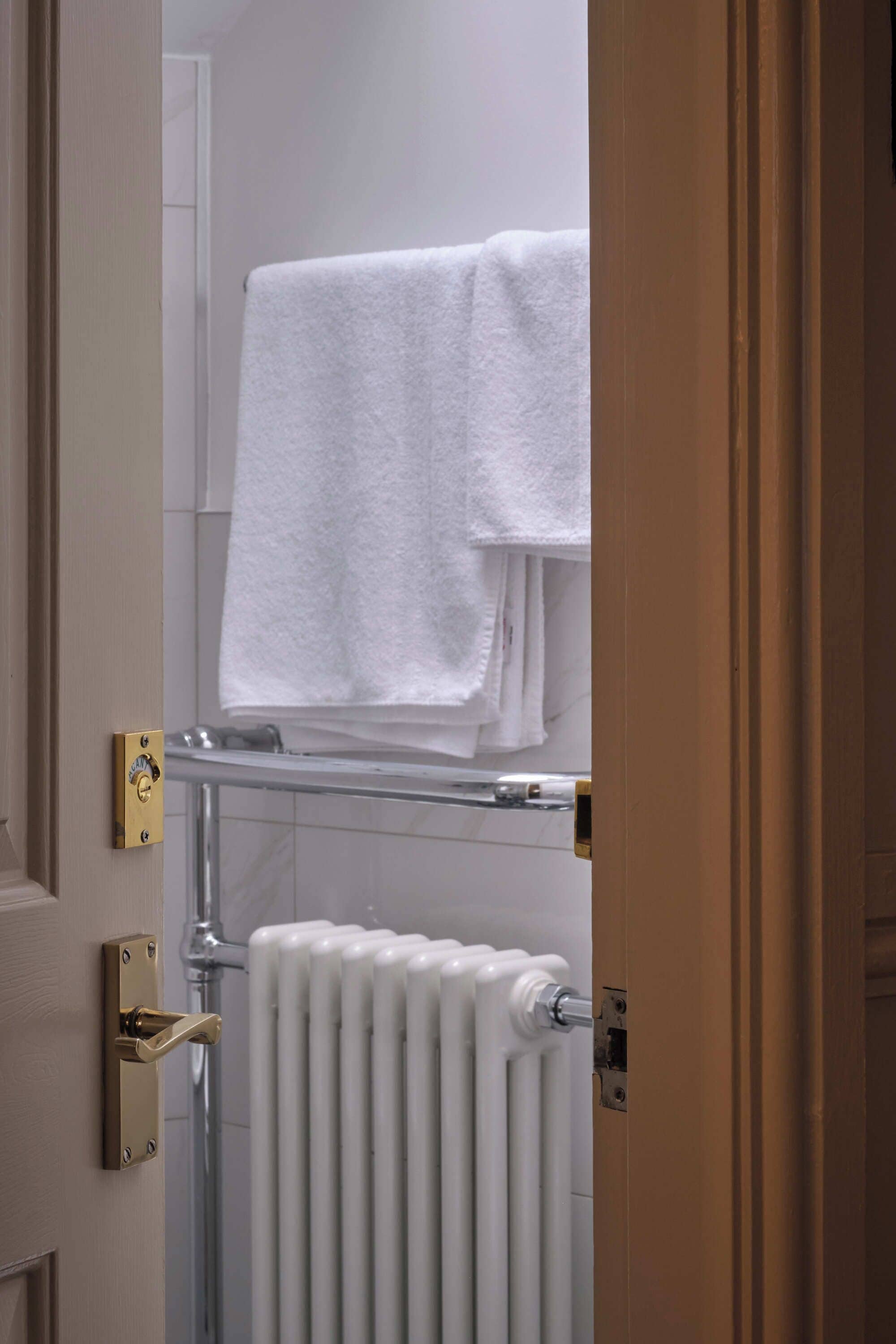 Un baño con toallero, radiador y puerta con picaporte de latón.