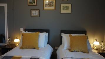 Habitación de hotel con dos camas, cada una con cabecera, mesita de noche con lámpara y cuadros en la pared.