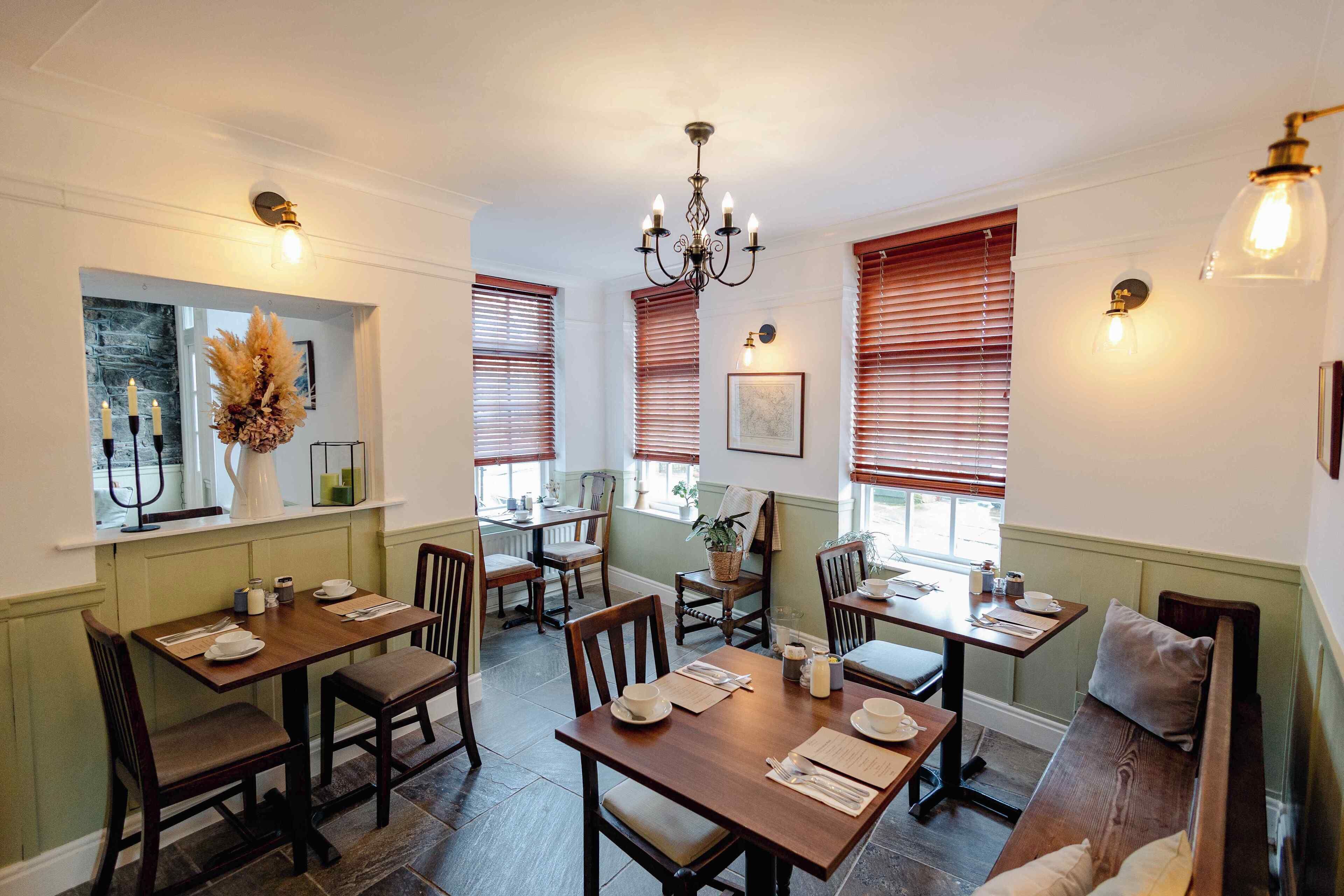 A dining area with wooden tables and chairs, a chandelier, and wall-mounted light fixtures.