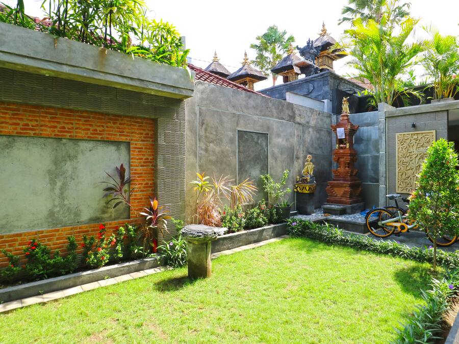 A courtyard with a brick wall, a small garden, a statue, and a traditional Balinese temple structure.