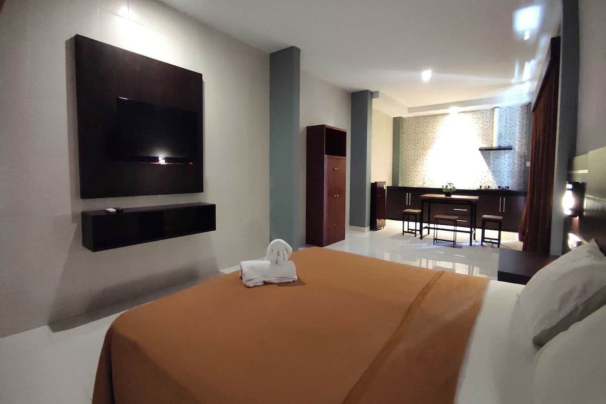 A hotel room with a bed, a flat-screen TV mounted on the wall, a small table with a plant, and a seating area with chairs.