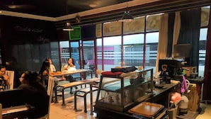 A cafe with tables and chairs, a counter with a coffee machine, and large windows. - Wisma Tobana (Jakarta)
