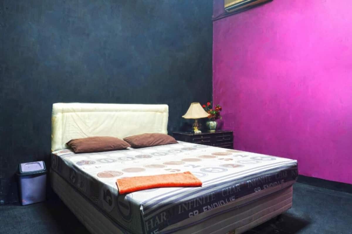 A bed with a patterned mattress, pillows, and a blanket. There is a nightstand with a lamp and a vase with flowers.