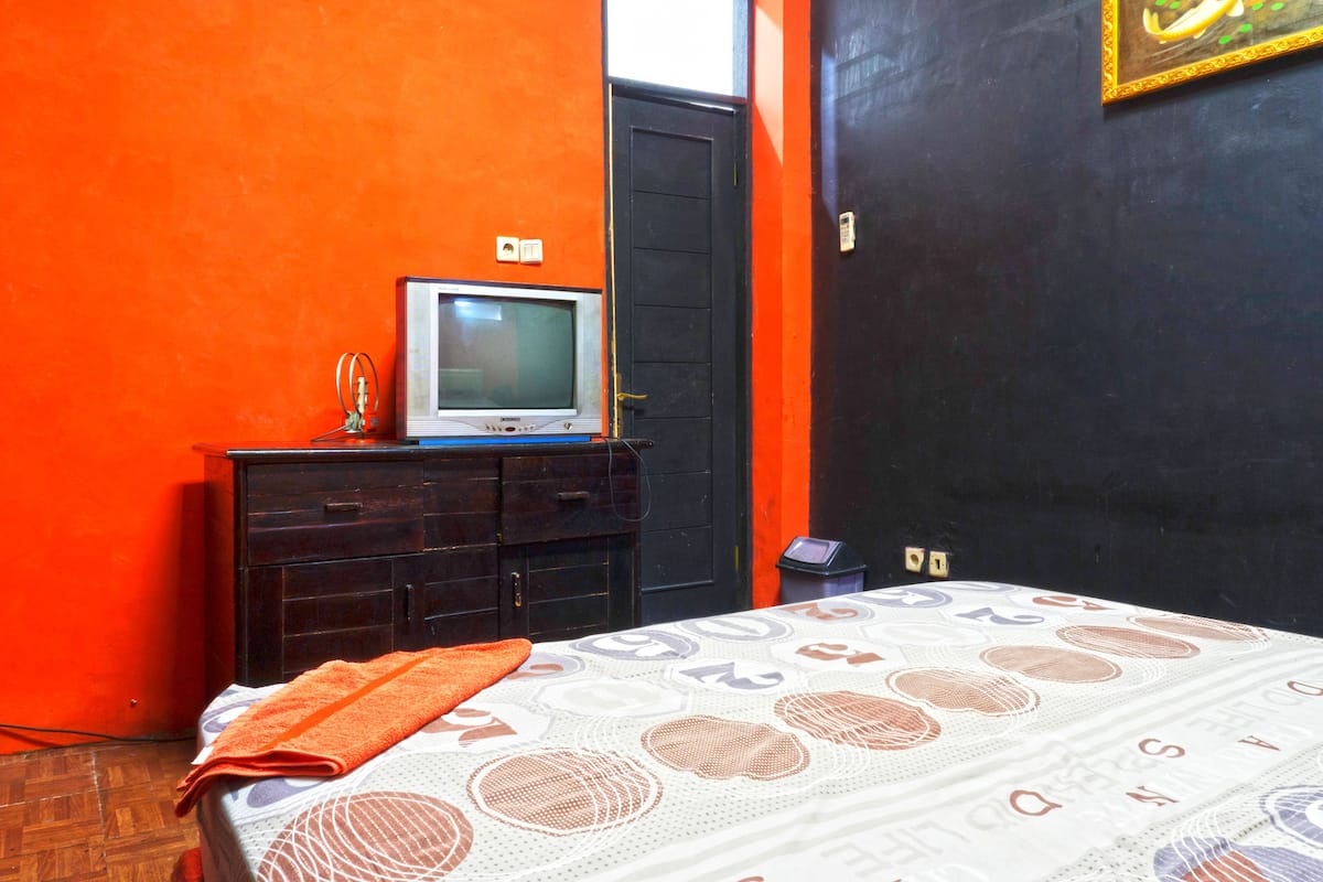 A room with a bed, a dresser, a television on top of the dresser, and a door.