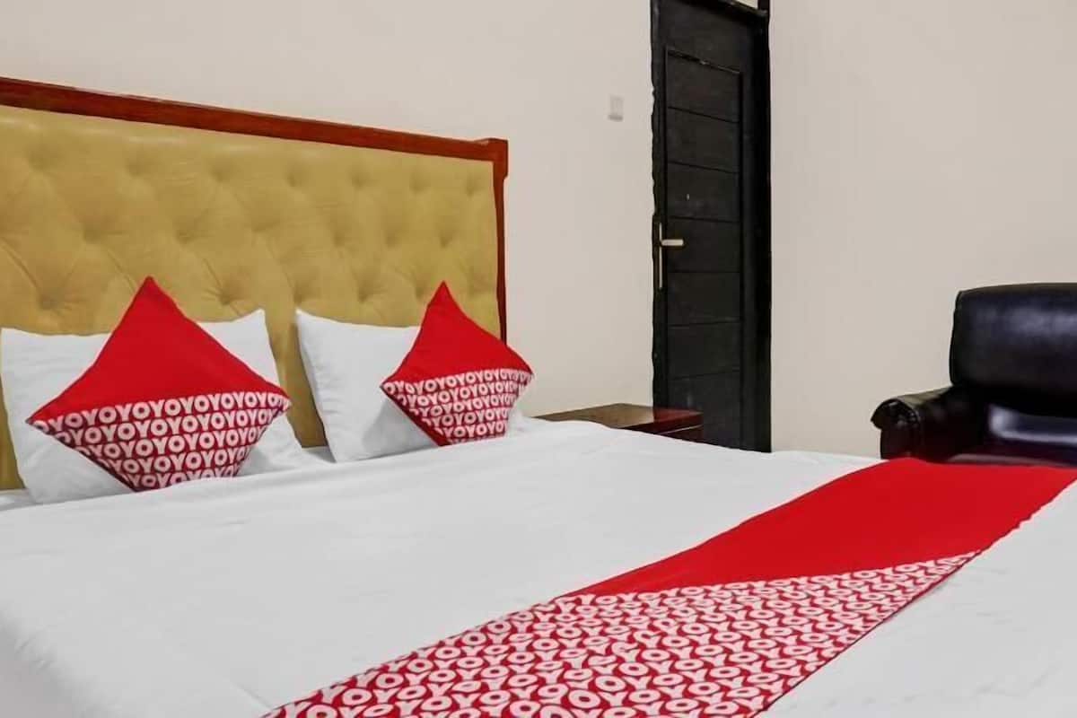 A bed with a red and white patterned bedspread, a tufted headboard, and two pillows with a red design.