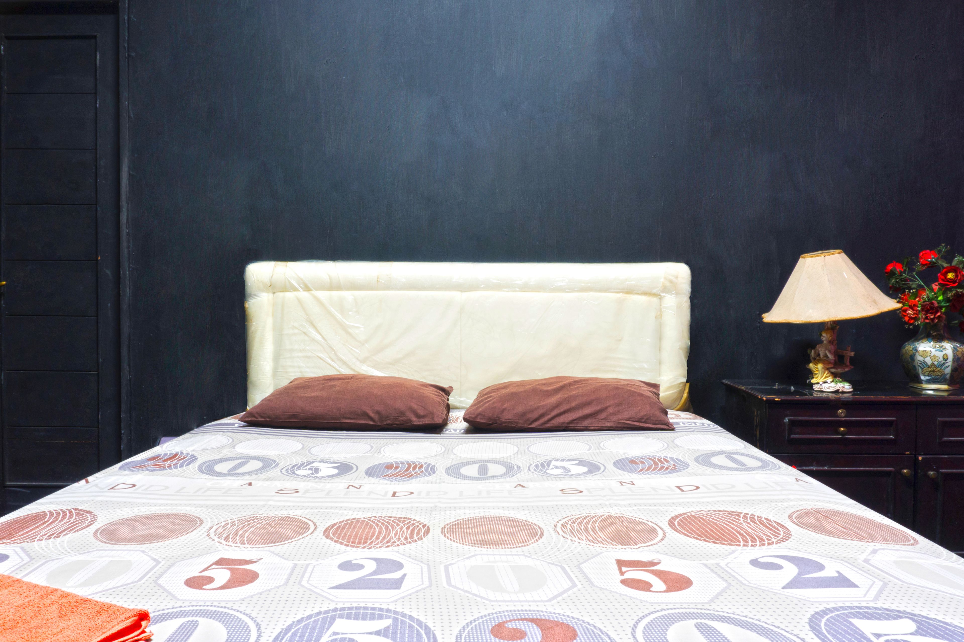 Ein Bett mit gemustertem Überwurf, zwei Kissen, ein Nachttisch mit Lampe und eine Vase mit Blumen.
