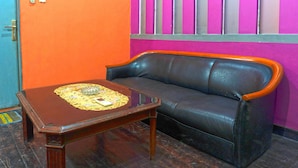 A room with a wooden coffee table, a black leather sofa, and a vibrant orange and pink wall.