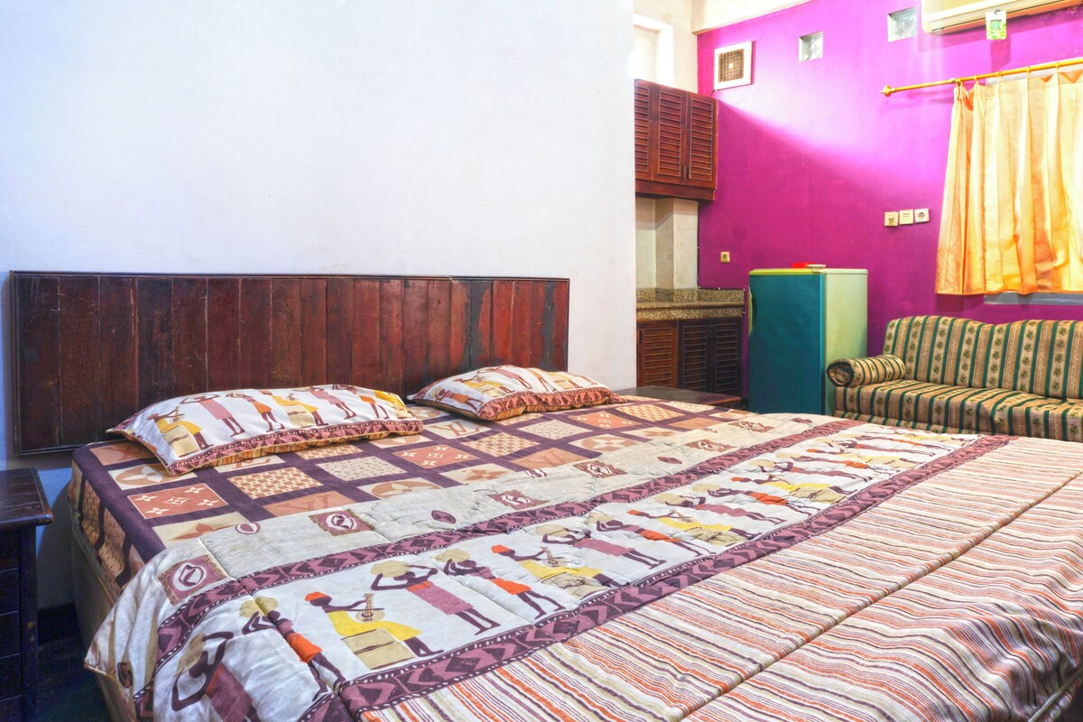 A bedroom with a wooden headboard, a patterned bedspread, a green cabinet, and a striped sofa.