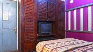 A room with a wooden wardrobe, a television on a shelf, and a bed with a patterned bedspread.