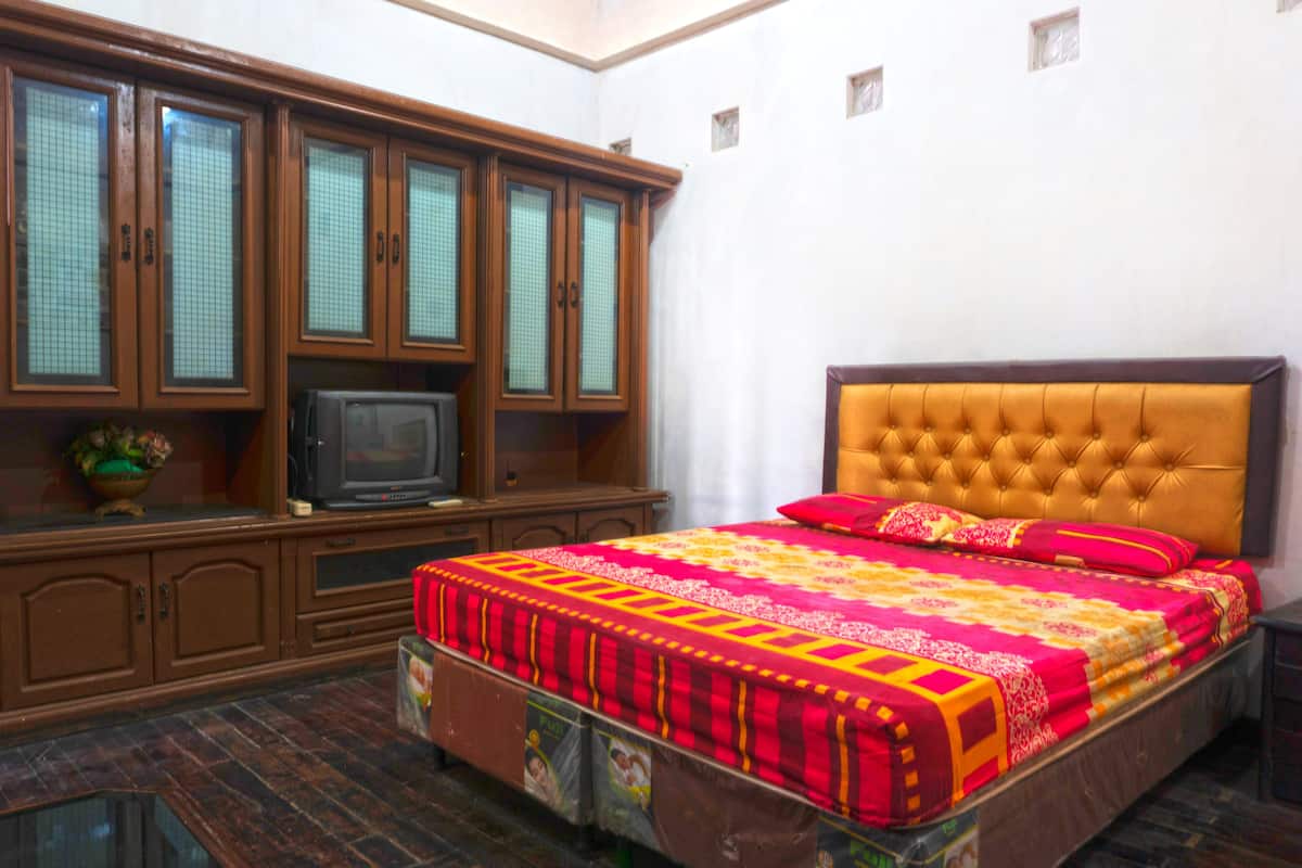Un dormitorio con una cama, televisión, armarios de madera y una mesita.