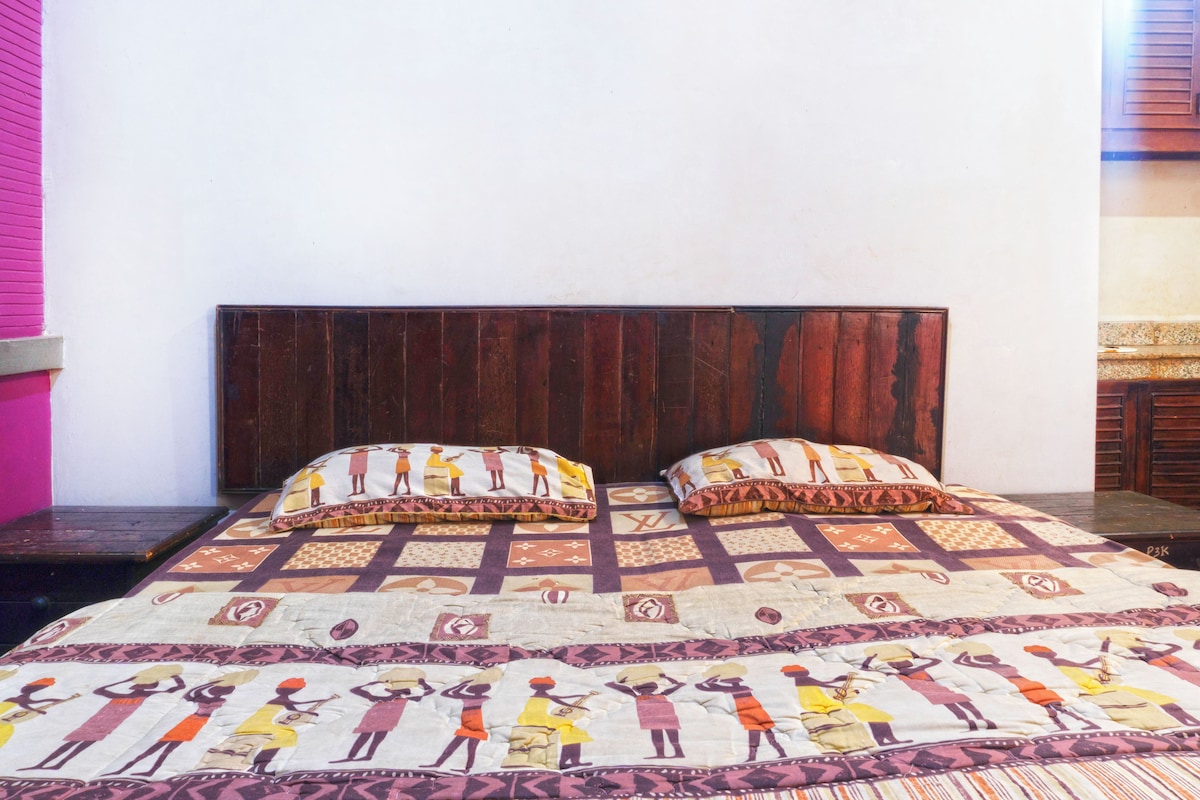 Una cama con colcha de motivos culturales, cabecera de madera y pared rosa.