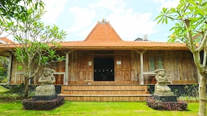 A traditional wooden house with a tiled roof, a central doorway, and two stone statues on either side.