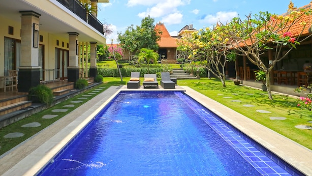 A swimming pool with lounge chairs, a garden with a variety of plants, and a traditional building with a tiled roof.