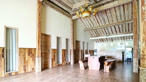A spacious room with wooden paneling, a wooden ceiling, and a chandelier. There is a reception desk and a counter with stools.