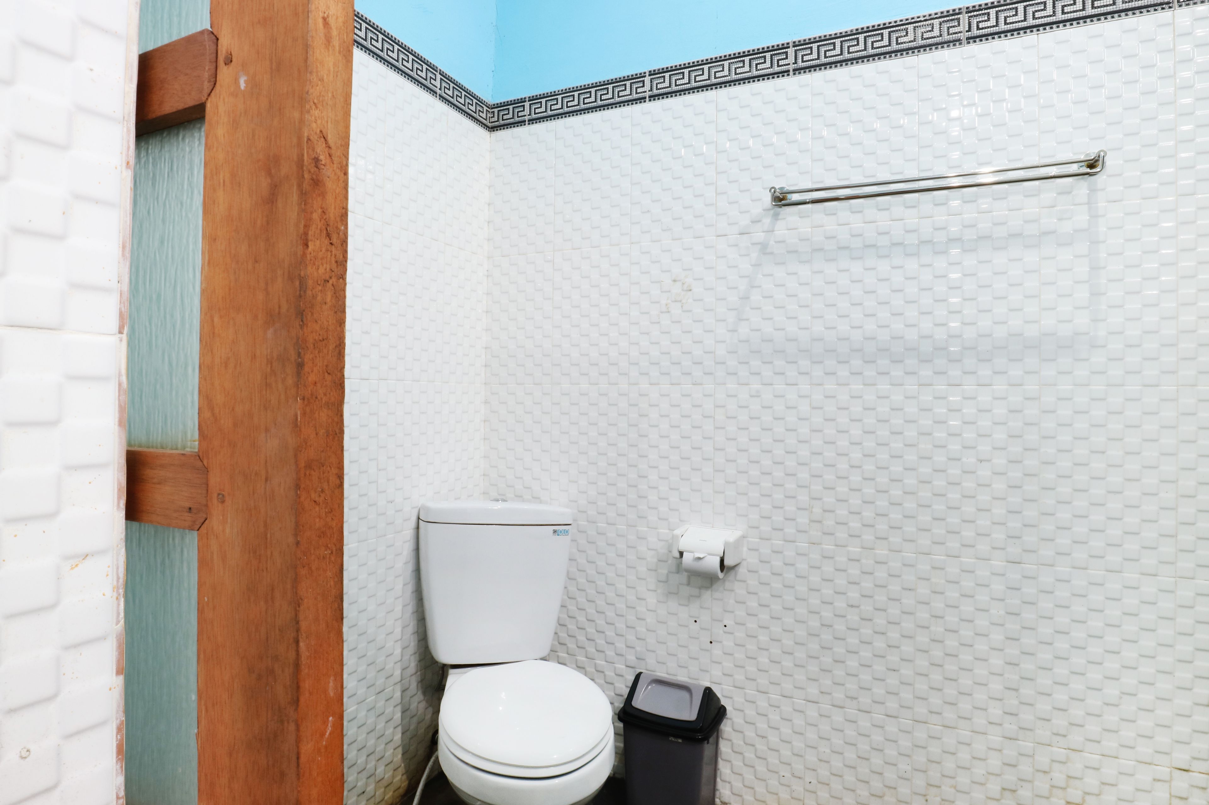Un baño con inodoro blanco, un cesto de basura y un perchero en una pared con azulejos.