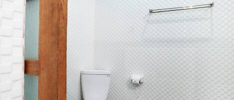 Un baño con inodoro blanco, un cesto de basura y un perchero en una pared con azulejos.