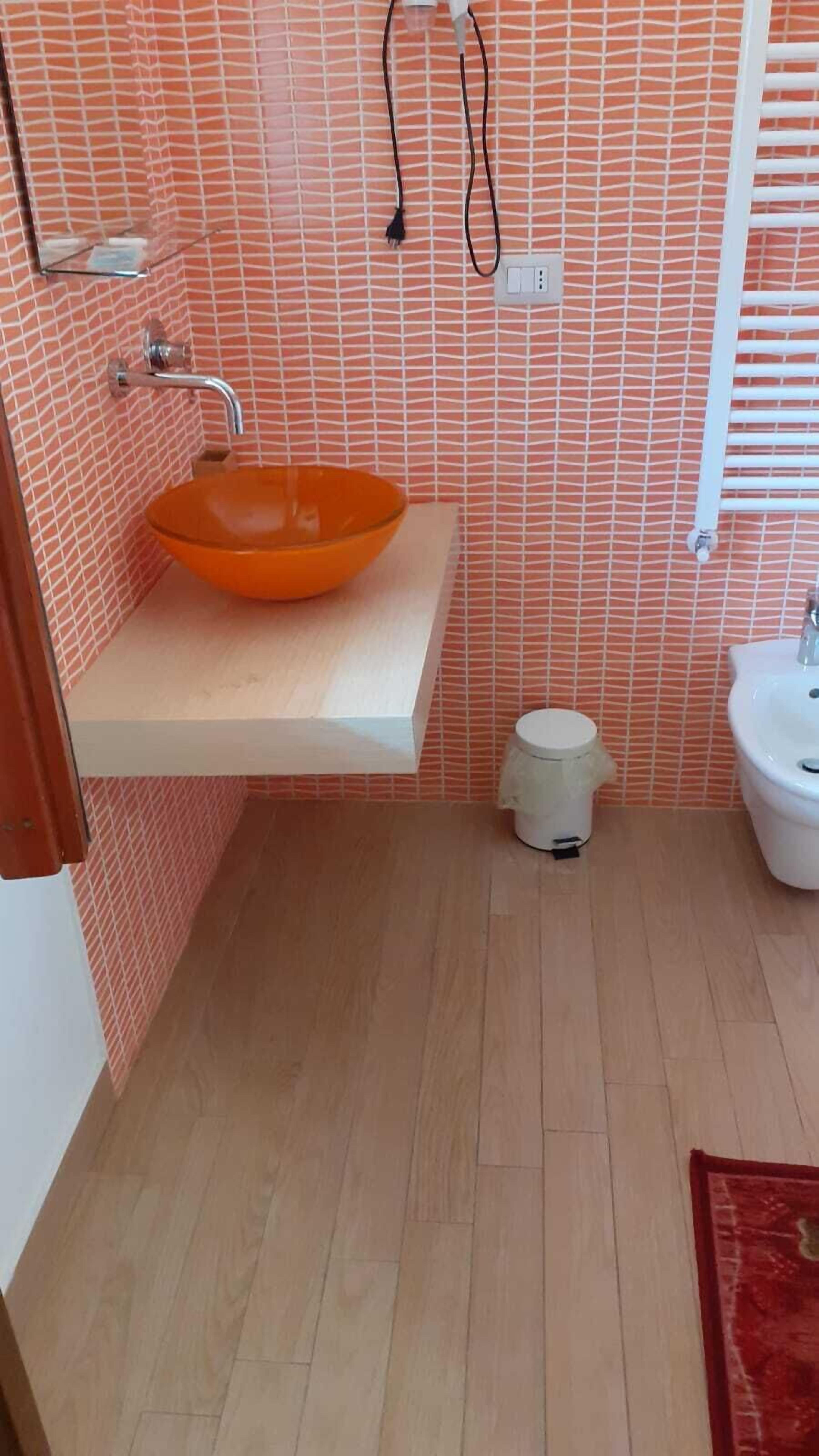 A bathroom with a glass bowl sink, a white pedestal sink, and a toilet.