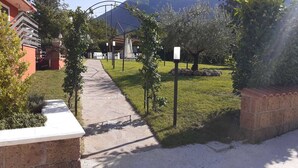 A pathway leading to a building with a mountain backdrop, surrounded by greenery and a brick wall. - B&B Villa Filomena (Serino)