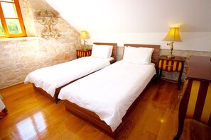 Two single beds with matching nightstands and lamps, set against a stone wall in a traditional room.
