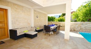Relax in a serene outdoor space with a sofa, dining table, and pool in the background.