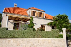Stunning two-story building with a covered porch area, surrounded by beautifully maintained hedges and a stone wall.