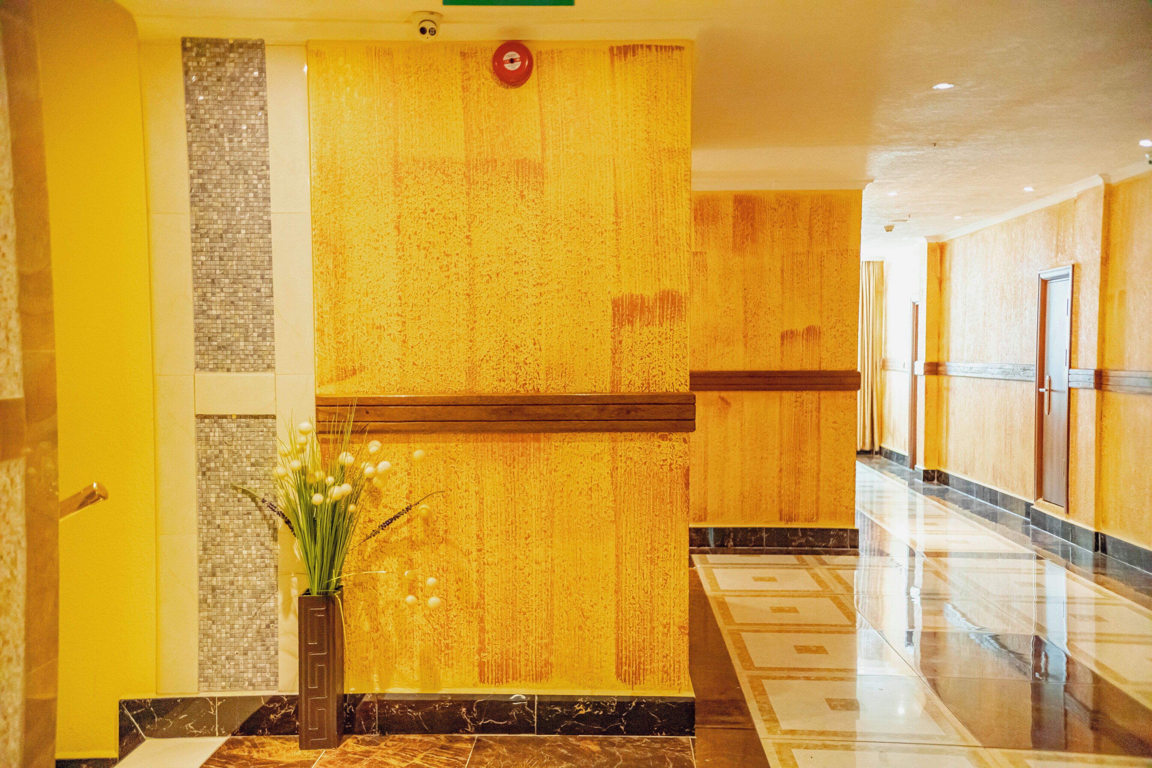 A hotel lobby with a reception desk, a decorative wall with a textured pattern, and a tiled floor.