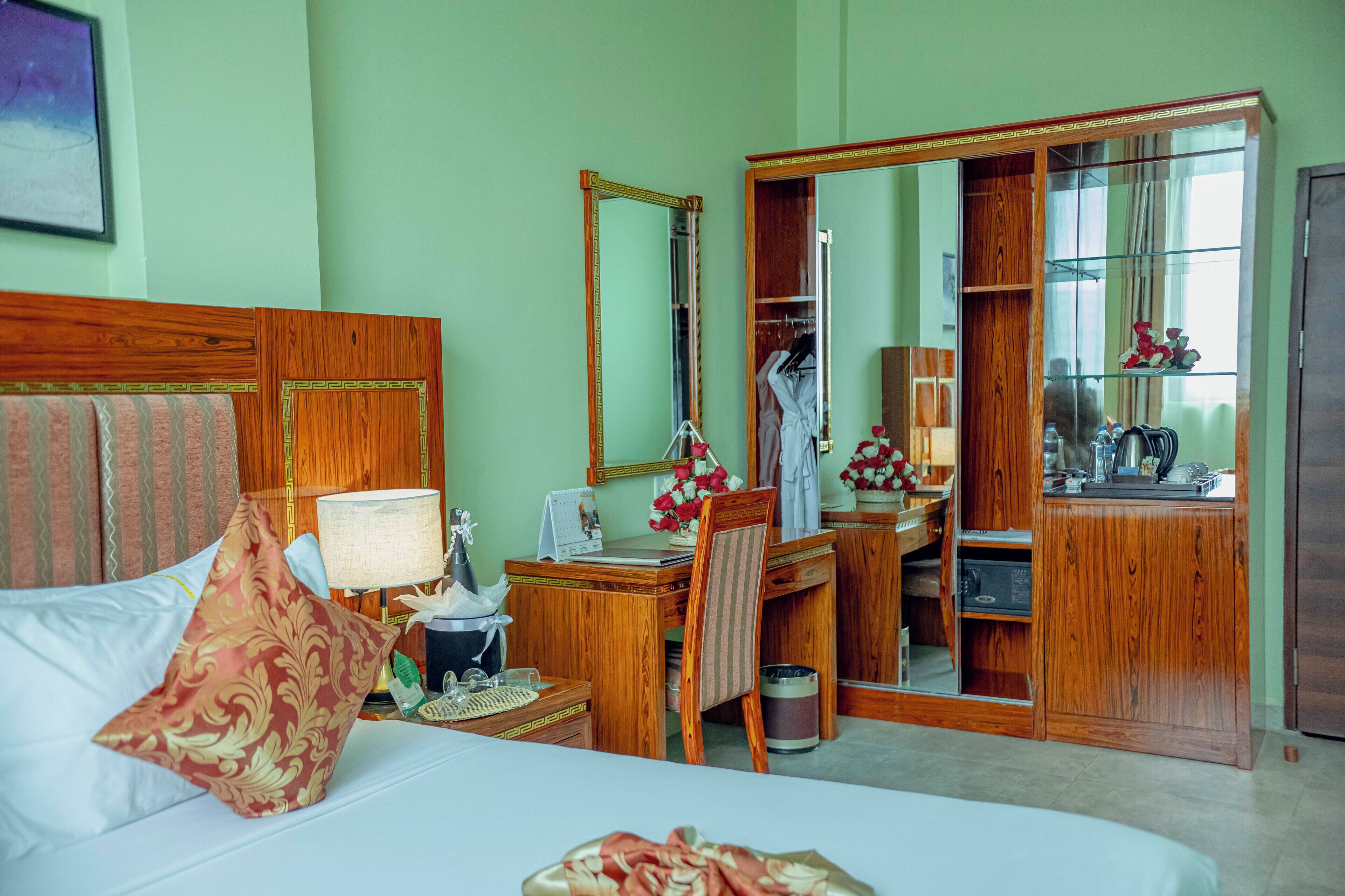 Een hotelkamer met een bed, een bureau, een spiegel, een kledingkast en een badkamer zichtbaar door een geopende deur.