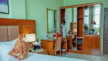 Een hotelkamer met een bed, een bureau, een spiegel, een kledingkast en een badkamer zichtbaar door een geopende deur.